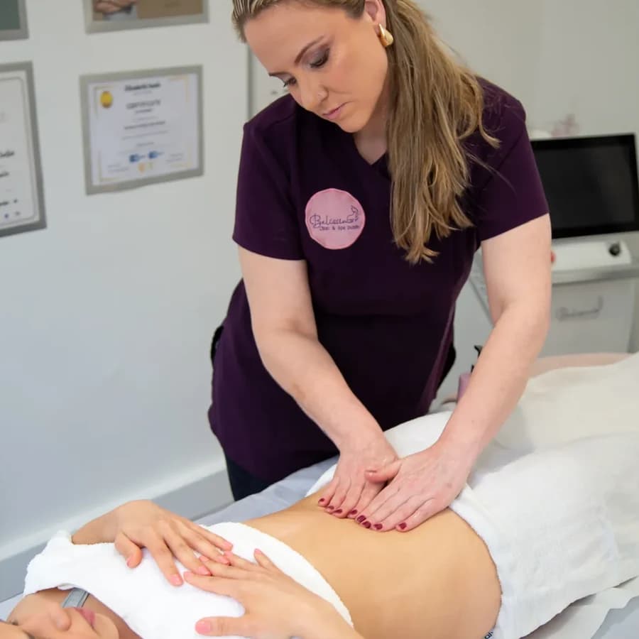 Andrea, in her plum uniform, resting her hands on a client's abdomen during a manual lymphatic drainage session